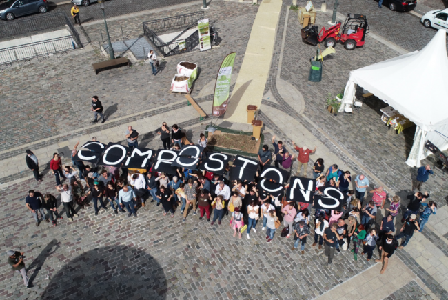 Une vue aérienne d'un groupe de personnes, tenant des lettres qui forment le mot "Compostons"